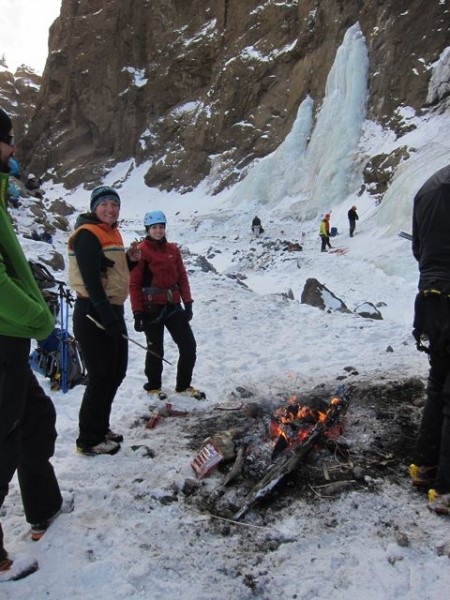 Climbers practice on the line of ice, while bystanders cook hot dogs.